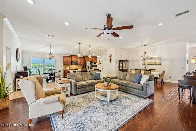 living area with crown molding, ceiling fan with notable chandelier, visible vents, and dark wood-style flooring