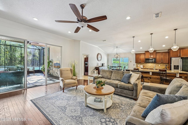 living area featuring visible vents, ornamental molding, hardwood / wood-style flooring, lofted ceiling, and ceiling fan