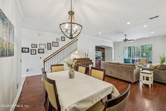 dining room with dark wood-type flooring, stairway, ornamental molding, ceiling fan with notable chandelier, and arched walkways