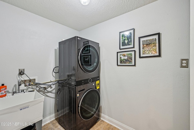 clothes washing area featuring baseboards, stacked washing maching and dryer, laundry area, a sink, and a textured ceiling