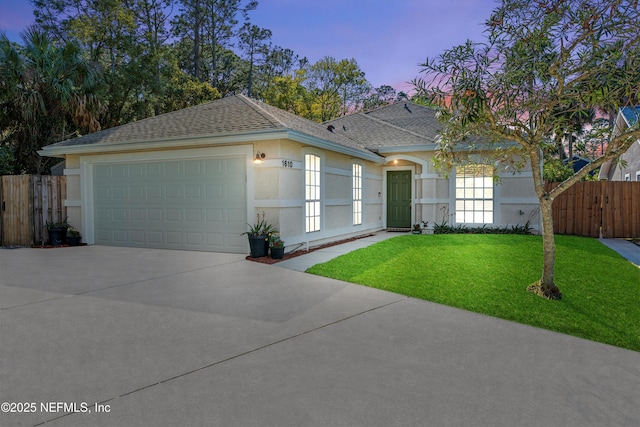 ranch-style home featuring stucco siding, driveway, a front lawn, fence, and roof with shingles