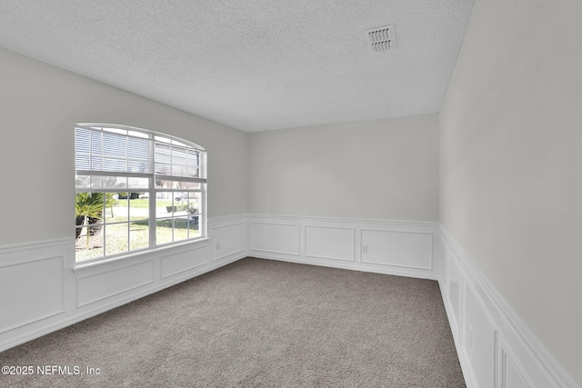 unfurnished room with a textured ceiling, wainscoting, carpet, and visible vents