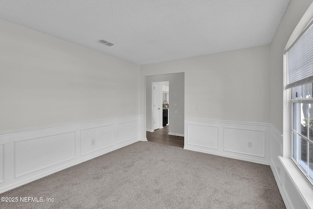 carpeted empty room featuring visible vents, a textured ceiling, and wainscoting