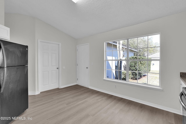 interior space featuring lofted ceiling, a textured ceiling, light wood-type flooring, and baseboards