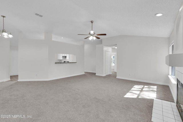 unfurnished living room with visible vents, light colored carpet, lofted ceiling, a tile fireplace, and ceiling fan with notable chandelier