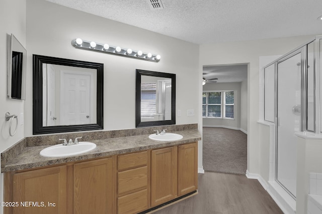 bathroom with double vanity, a stall shower, visible vents, a textured ceiling, and a sink