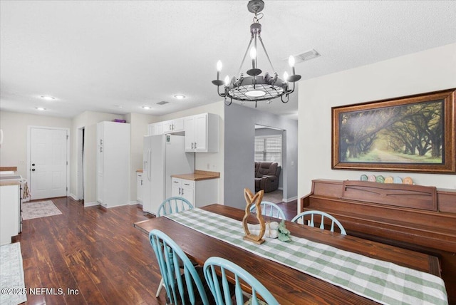 dining area featuring dark wood-style floors, visible vents, an inviting chandelier, a textured ceiling, and baseboards