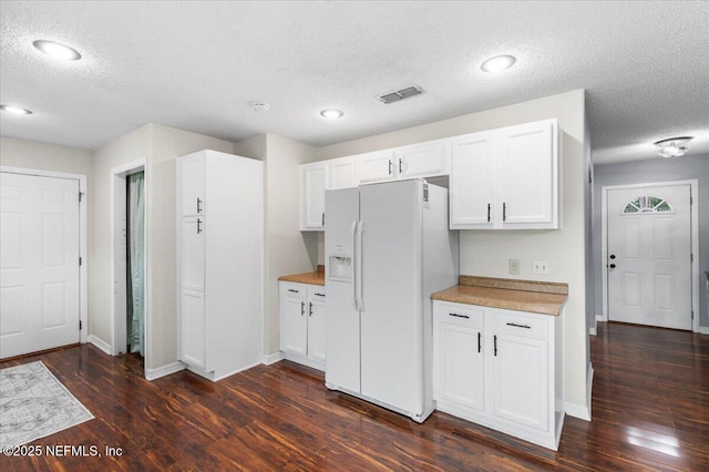 kitchen with visible vents, white cabinets, dark wood-style floors, light countertops, and white fridge with ice dispenser