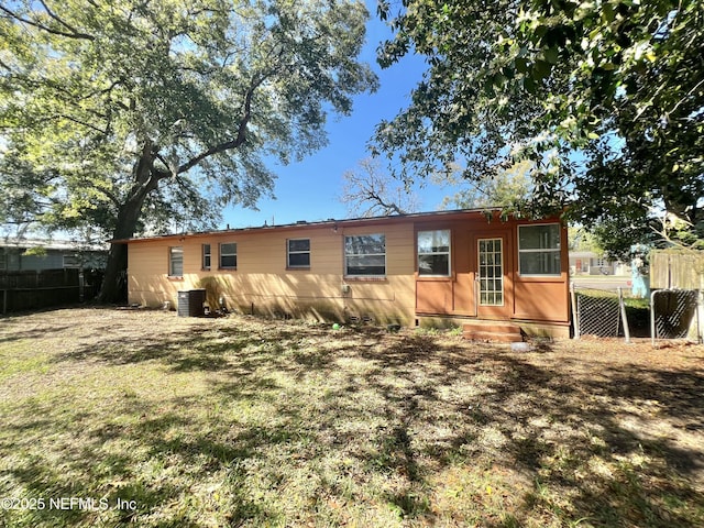 rear view of house featuring fence, a lawn, and central air condition unit