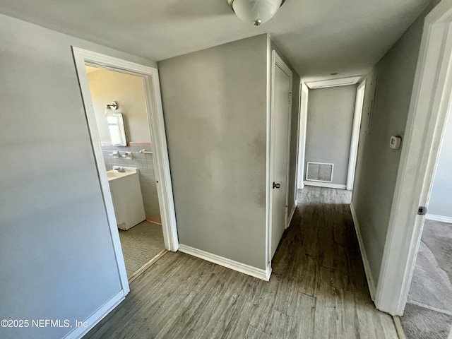 corridor featuring wood finished floors, visible vents, and tile walls