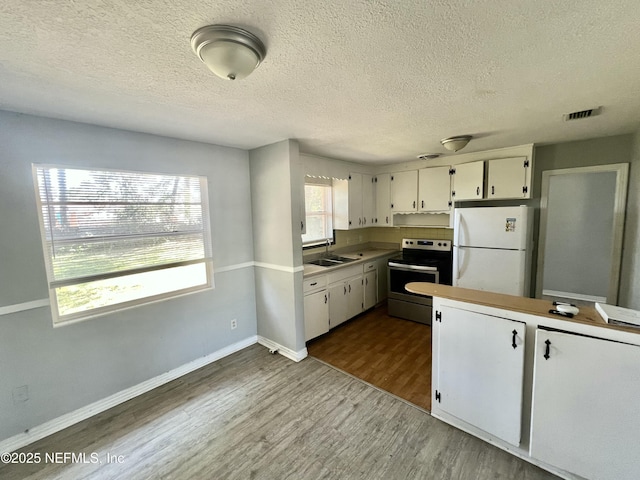 kitchen with electric stove, dark wood-type flooring, freestanding refrigerator, white cabinetry, and a sink