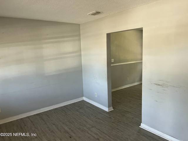 unfurnished room with a textured ceiling, dark wood-type flooring, visible vents, and baseboards