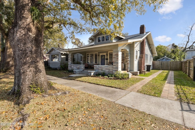 bungalow-style home with stone siding, a porch, a chimney, and fence