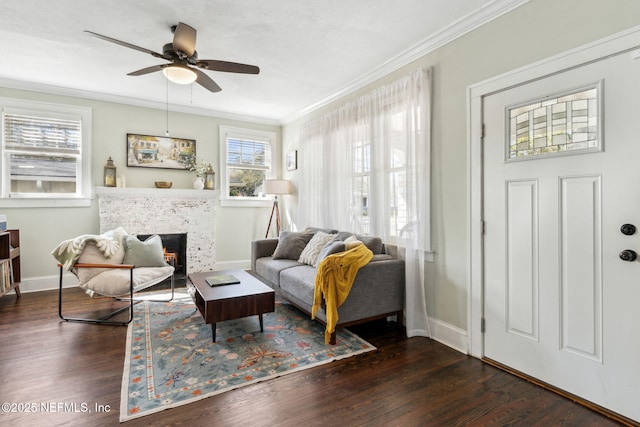 living room with a warm lit fireplace, baseboards, a ceiling fan, ornamental molding, and dark wood-type flooring