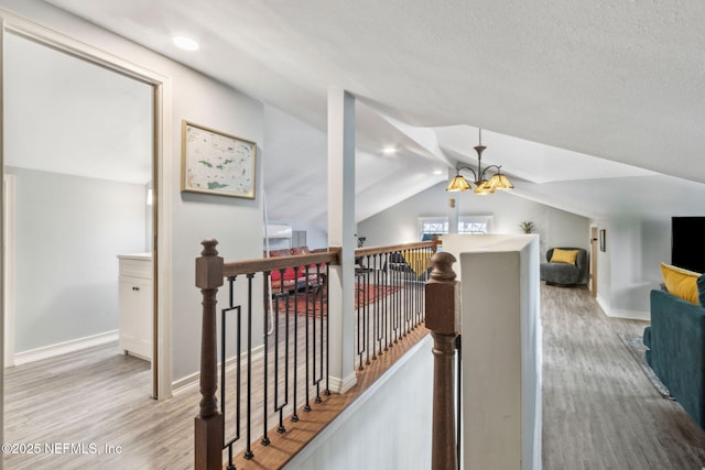 hall with vaulted ceiling, wood finished floors, an upstairs landing, and a chandelier