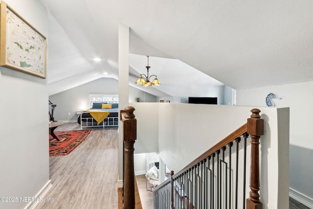 stairs with a notable chandelier, vaulted ceiling, baseboards, and wood finished floors