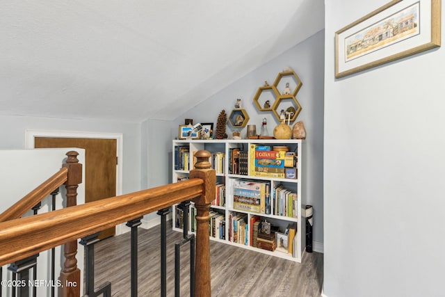 corridor with vaulted ceiling, wood finished floors, and an upstairs landing