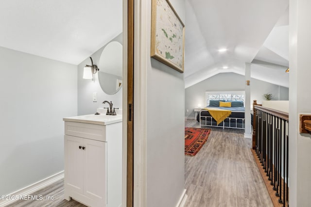 bathroom featuring vaulted ceiling, wood finished floors, vanity, and baseboards