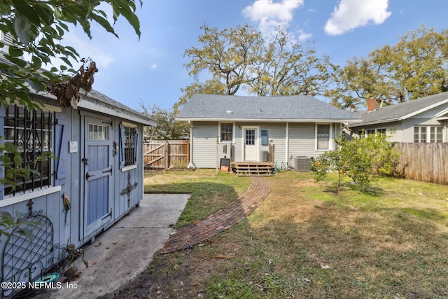 back of property with central AC, fence, an outdoor structure, and a lawn