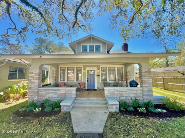 view of front of house with a porch, fence, stone siding, and a chimney