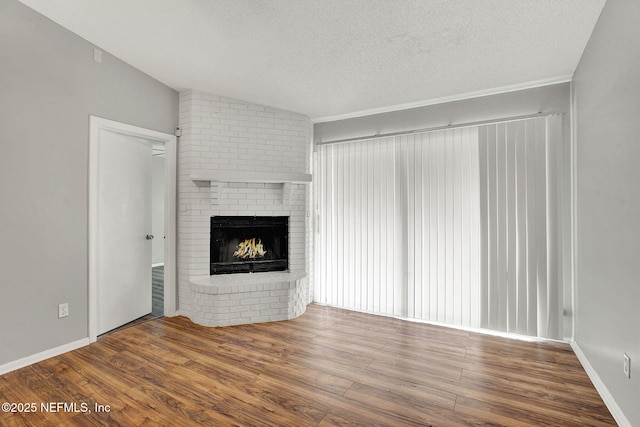 unfurnished living room with baseboards, wood finished floors, vaulted ceiling, a textured ceiling, and a fireplace