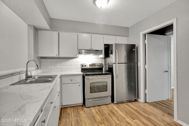 kitchen with under cabinet range hood, stainless steel appliances, a sink, light wood-style floors, and white cabinets