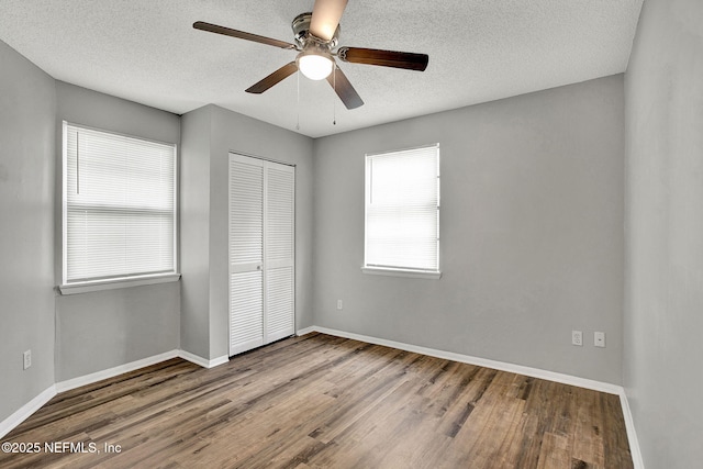 unfurnished bedroom featuring a closet, a textured ceiling, baseboards, and wood finished floors