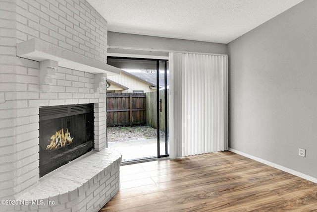 unfurnished living room featuring a brick fireplace, a textured ceiling, baseboards, and wood finished floors