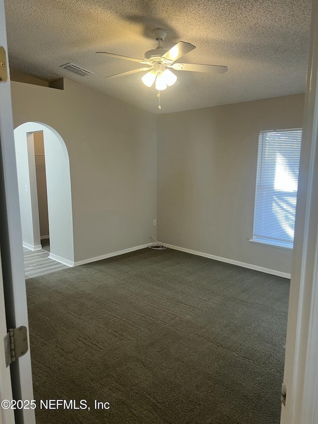 spare room with visible vents, arched walkways, a ceiling fan, dark colored carpet, and a textured ceiling