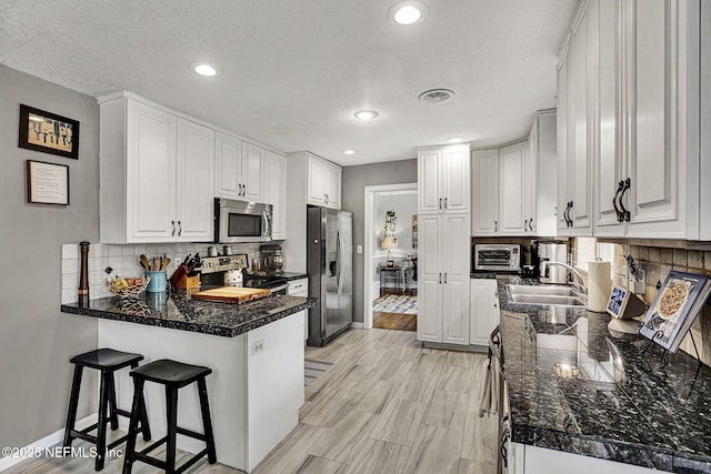 kitchen with visible vents, appliances with stainless steel finishes, a sink, a peninsula, and a kitchen bar