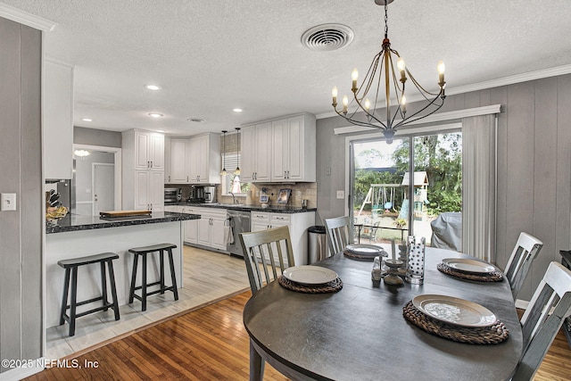 dining area with a textured ceiling, light wood-style flooring, visible vents, and crown molding