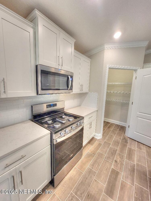 kitchen featuring decorative backsplash, ornamental molding, appliances with stainless steel finishes, wood finish floors, and white cabinetry