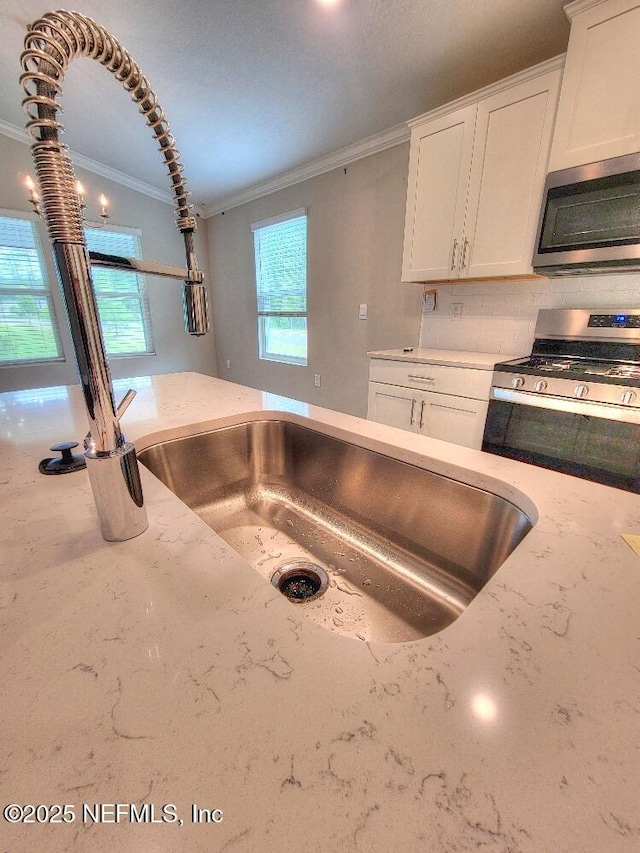 kitchen with stainless steel appliances, a healthy amount of sunlight, white cabinetry, and ornamental molding