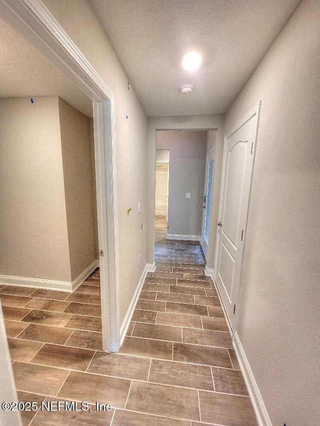 corridor featuring baseboards, a textured ceiling, and wood finish floors