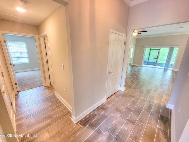 hallway featuring wood finish floors, crown molding, and baseboards