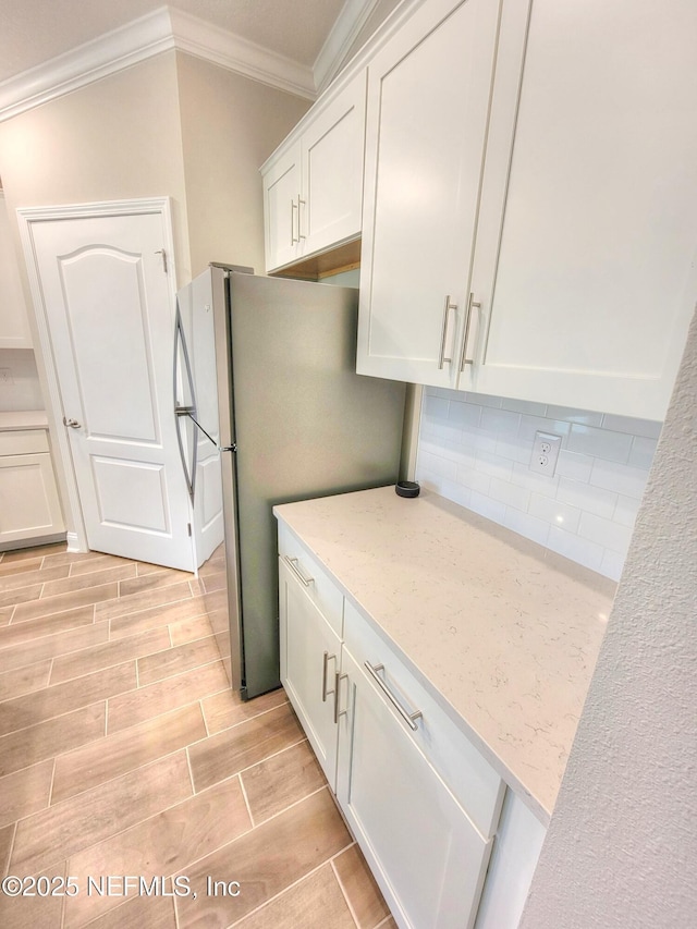 kitchen with light stone counters, wood finish floors, decorative backsplash, ornamental molding, and white cabinets