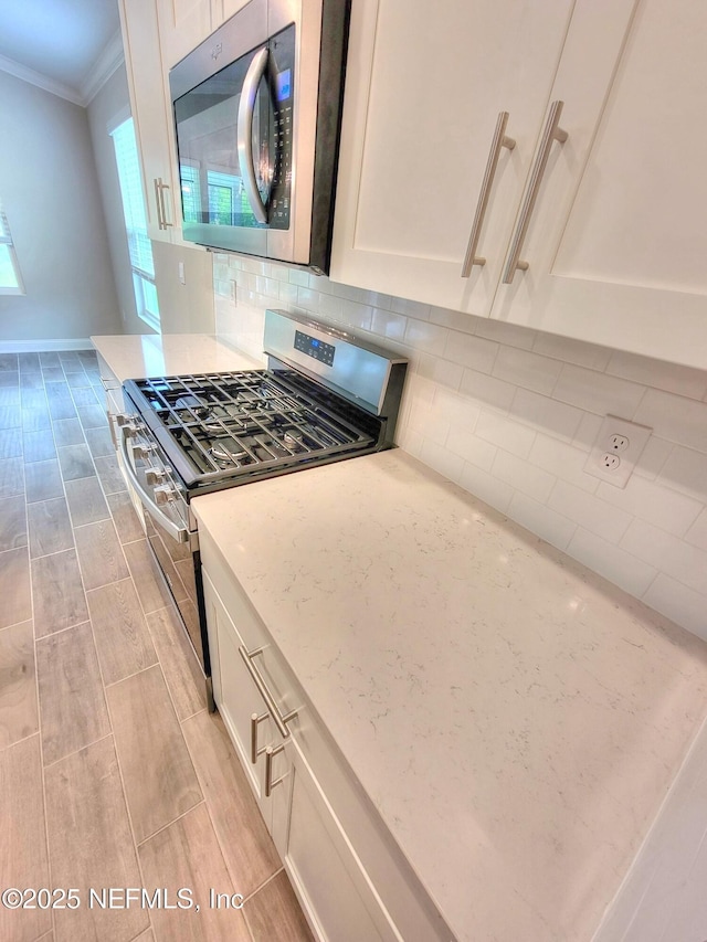 kitchen with stainless steel appliances, decorative backsplash, ornamental molding, white cabinets, and light stone countertops