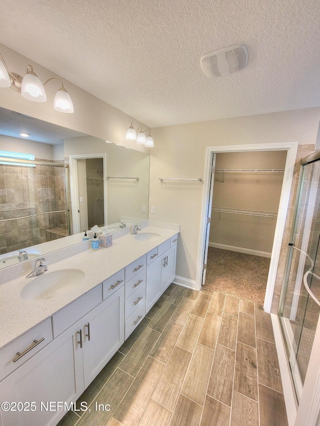 bathroom with double vanity, a shower stall, a spacious closet, and a sink