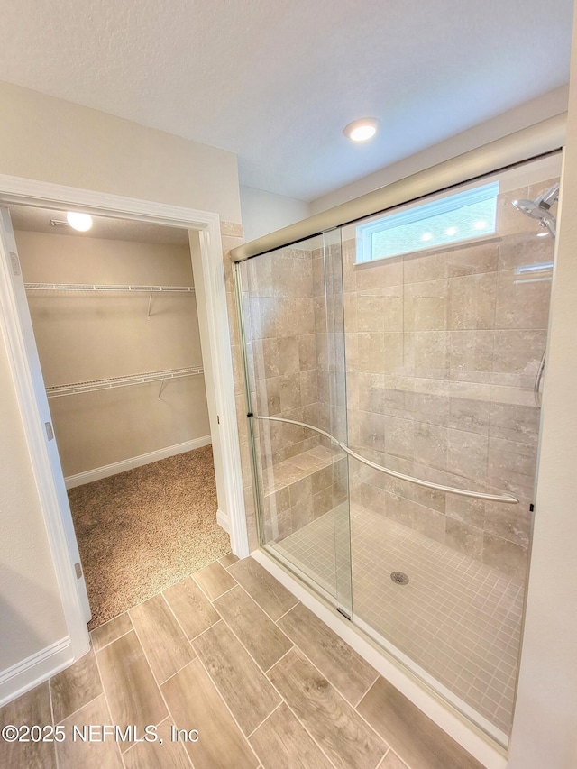 bathroom with a shower stall, baseboards, and a spacious closet