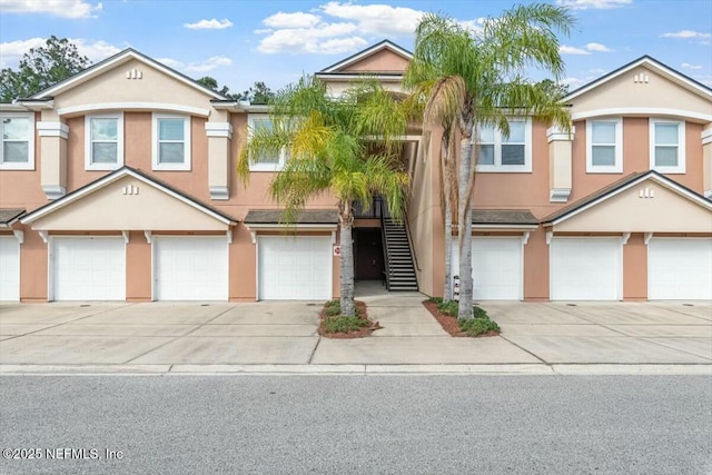 townhome / multi-family property with driveway, a garage, stairs, and stucco siding