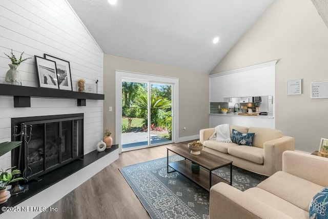 living room featuring recessed lighting, a large fireplace, wood finished floors, high vaulted ceiling, and baseboards