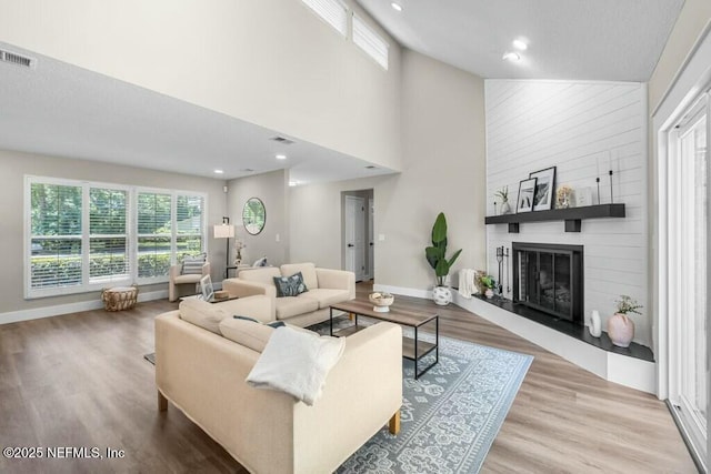 living area with a large fireplace, wood finished floors, visible vents, and baseboards