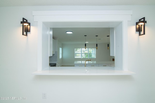 kitchen featuring decorative light fixtures, light countertops, white cabinets, a sink, and a peninsula