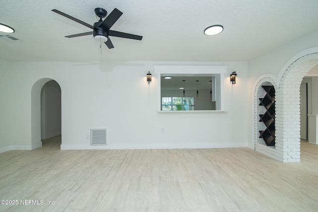 unfurnished room with arched walkways, visible vents, a textured ceiling, and wood finished floors