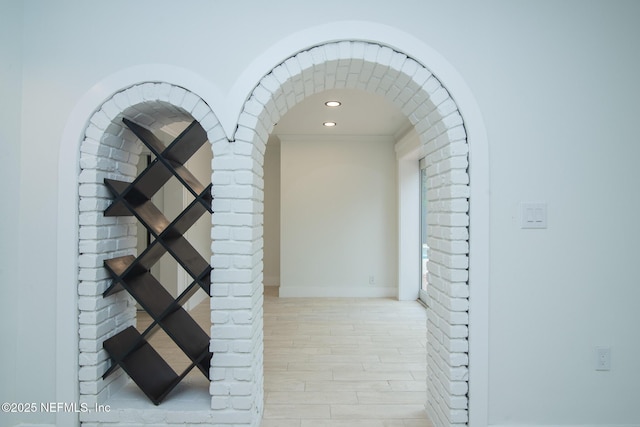 corridor with brick wall, recessed lighting, wood finished floors, and baseboards