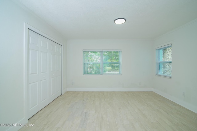 unfurnished bedroom with light wood finished floors, baseboards, a closet, and ornamental molding