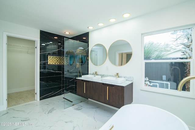 full bath with a sink, marble finish floor, tiled shower, a spacious closet, and double vanity