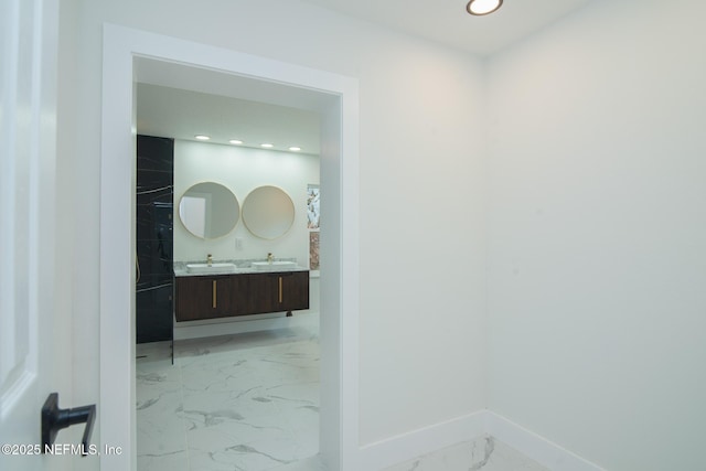 bathroom featuring double vanity, marble finish floor, baseboards, and a sink