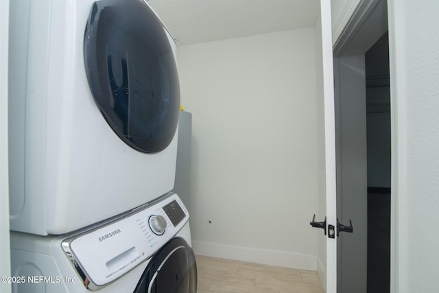 washroom with laundry area, light wood finished floors, stacked washing maching and dryer, and baseboards