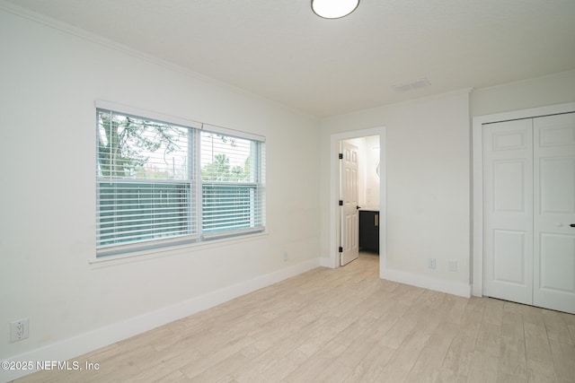 unfurnished bedroom featuring connected bathroom, baseboards, light wood-style floors, ornamental molding, and a closet